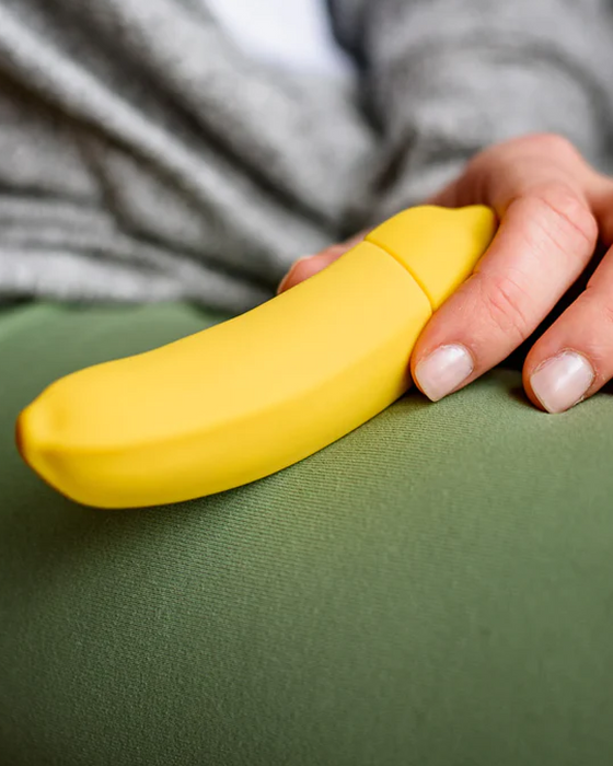 Banana Emojibator Vibrator held in woman's hand against her green pants 