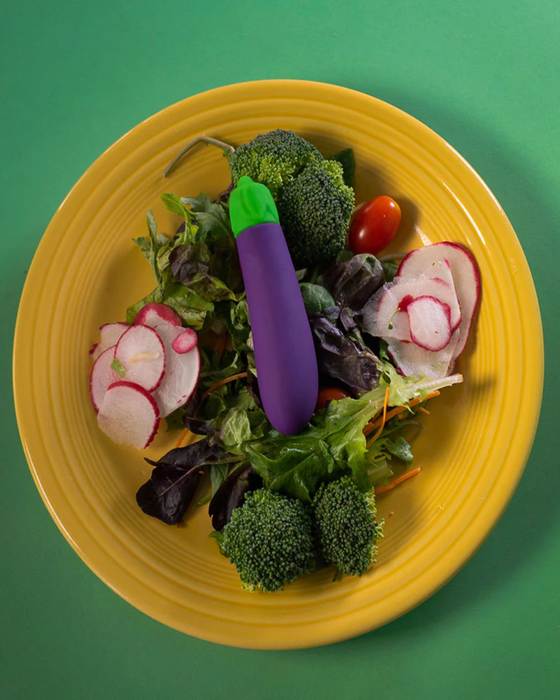 Eggplant Emojibator Vibrator on yellow plate on top of vegetables 