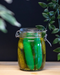 Pickle Emojibator Vibrator in pickle jar with pickled and greenery in the background 