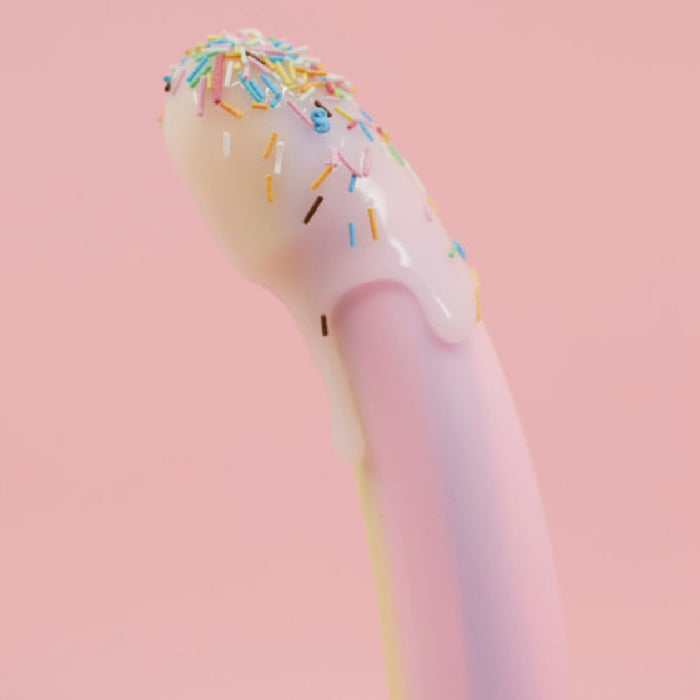 A pastel Fantasia Smooth 7 inch Glow in the Dark Silicone Dildo with Suction Cup is coated in white icing and colorful sprinkles, set against a pink background.