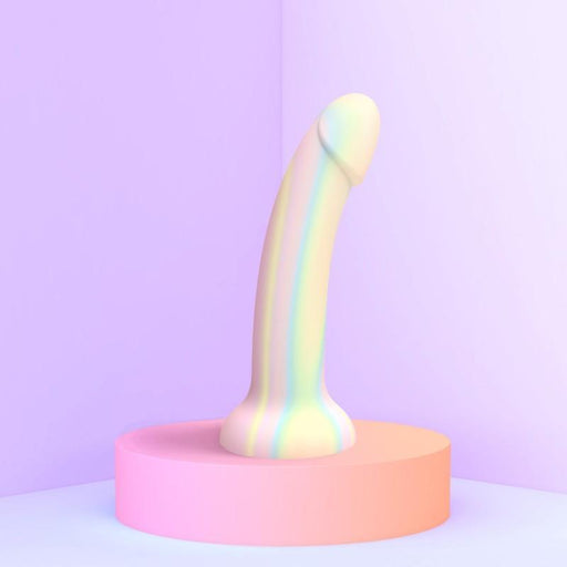 The Fantasia Smooth 7 inch Glow in the Dark Silicone Dildo with Suction Cup, featuring pastel rainbow stripes, stands upright on a pink platform against a soft purple backdrop in a bright, minimalistic scene.