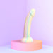 The Fantasia Smooth 7 inch Glow in the Dark Silicone Dildo with Suction Cup, featuring pastel rainbow stripes, stands upright on a pink platform against a soft purple backdrop in a bright, minimalistic scene.