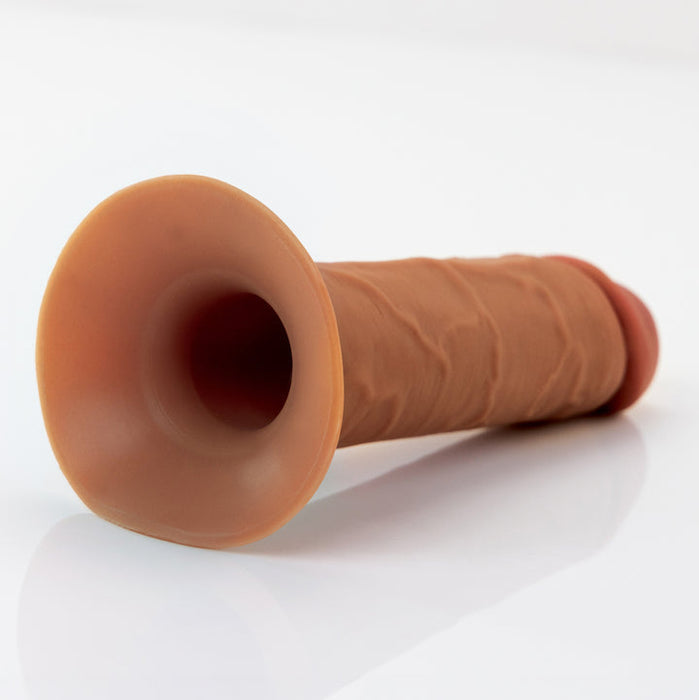 The Fantasy X-Tensions Elite Hollow 5 Inch Silicone Dildo & Strap-On Harness in Chocolate, made from dual-density silicone with a flared opening, rests on a white surface.