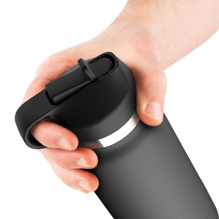 A hand is holding a black travel mug with a snap-on lid and a carrying handle, reminiscent of the discreet design of the Fuck Flask Pussy Stroker Disguised as a Water Bottle - Vanilla by Pipedream Products. The mug has a sleek, matte finish and a silver band around the top. The background is plain white.