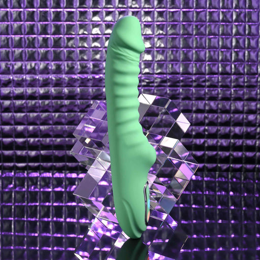 The Full Throttle Warming Waterproof Silicone Vibrator stands upright on a clear acrylic block, set against a shiny purple textured background that reflects light.