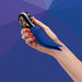 A hand with red-painted nails holds the Fun Factory Volta Rechargeable External Vibrator in Petrol Blue, showcasing its powerful motor. Its buttons suggest versatile external stimulation functions, set against a blue geometric pattern that complements its design.