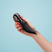 A hand with red nail polish holds a black, sleek Fun Factory Volta Rechargeable External Vibrator in Petrol Blue, embodying cutting-edge German design against a light blue background.