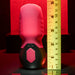 The Body Kisses Red Suction Masturbator and Vibrator by Evolved Novelties, featuring a red and black cylindrical design with a textured silicone surface, stands next to a yellow tape measure indicating a height of approximately 6 inches. The background showcases an eye-catching red illuminated area, creating a dramatic lighting effect.