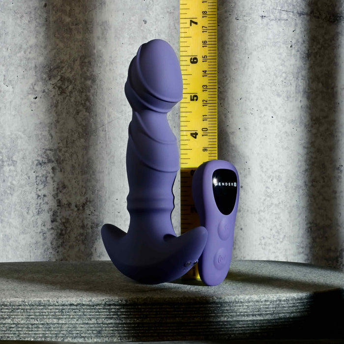 The Ring It Remote Control Rimming Vibrating Prostate Plug in purple stands upright beside a yellow measuring tape and its remote control, all set against a textured gray background.