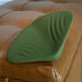 A green Gender X Pleasure Pad Rechargeable Grinding Pad & Stroker with textured ridges sits on a tan leather tufted ottoman.