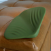 A green Gender X Pleasure Pad Rechargeable Grinding Pad & Stroker with textured ridges sits on a tan leather tufted ottoman.