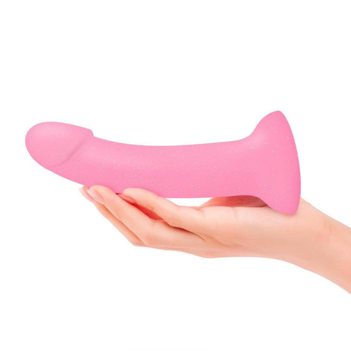 A hand holds the Glitzy Smooth 7 inch Pink Sparkle Silicone Dildo with Suction Cup against a plain white background.