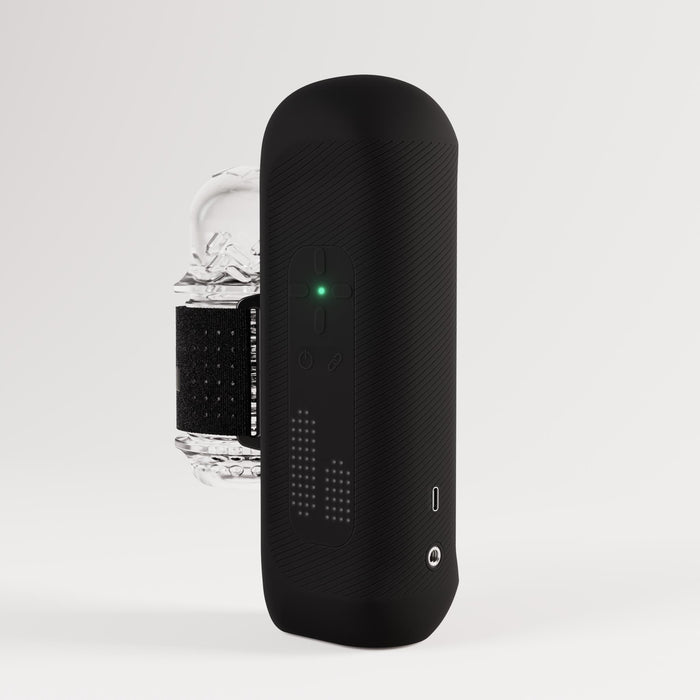 The Handy 2 Interactive Automatic Masturbator, a sleek black handheld male sex toy with textured sides, buttons, a green indicator light, and digital display, is shown in front of a clear ice cube on a plain white background.