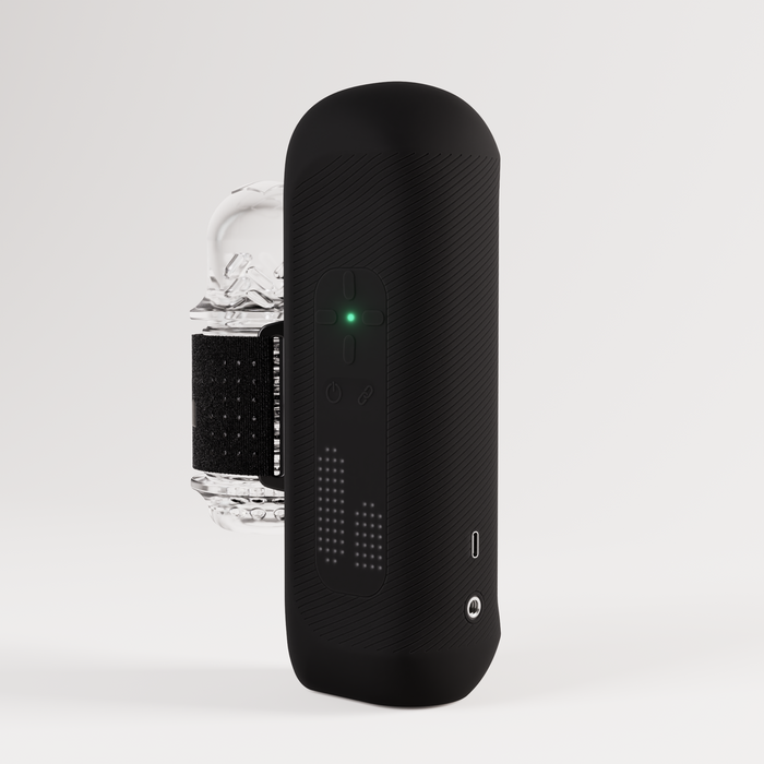 The Handy 2 Interactive Automatic Masturbator, a sleek black handheld male sex toy with textured sides, buttons, a green indicator light, and digital display, is shown in front of a clear ice cube on a plain white background.