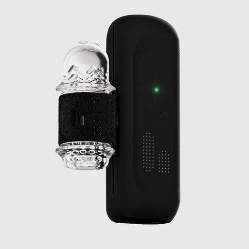 The Handy 2 Interactive Automatic Masturbator, a sleek black app-controlled device with a green indicator light, sits next to its clear textured silicone sleeve and adjustable black strap against a plain light background.