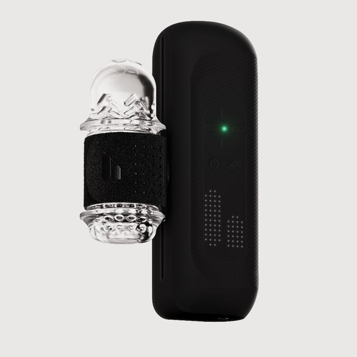 The Handy 2 Interactive Automatic Masturbator, a sleek black app-controlled device with a green indicator light, sits next to its clear textured silicone sleeve and adjustable black strap against a plain light background.