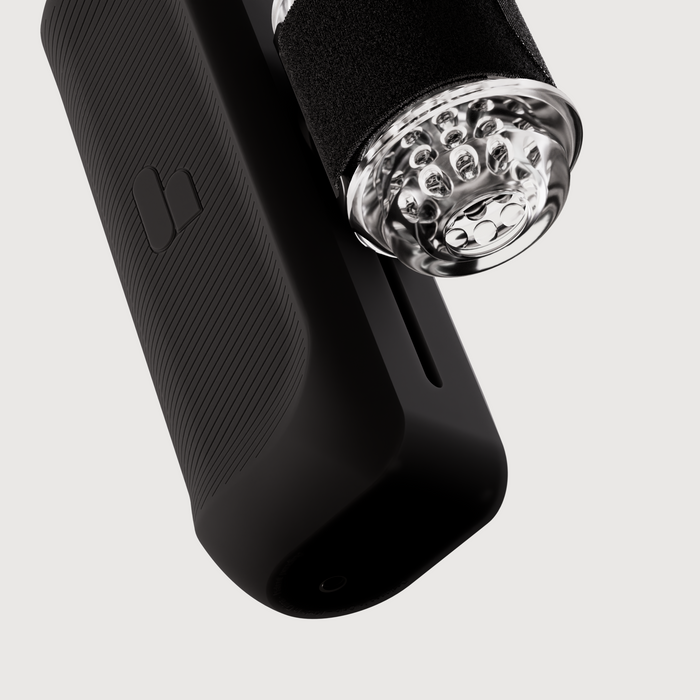 A close-up of The Handy 2 Interactive Automatic Masturbator, a black textured device with a transparent cylindrical attachment featuring multiple small round parts inside, shown against a plain white background.