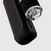 A close-up of The Handy 2 Interactive Automatic Masturbator, a black textured device with a transparent cylindrical attachment featuring multiple small round parts inside, shown against a plain white background.