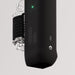 Close-up of a black, cylindrical portable speaker with display, USB-C port, and 3.5mm jack; The Handy 2 Interactive Automatic Masturbator is attached to the side along with a transparent water bottle featuring a black strap.