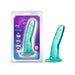 The Hard n' Happy Slim 5 inch Teal Mini Dildo with Suction Cup stands upright beside its box, which shows the product and icons for its 5-inch length, soft feel, body-safe material, and strong suction cup base.