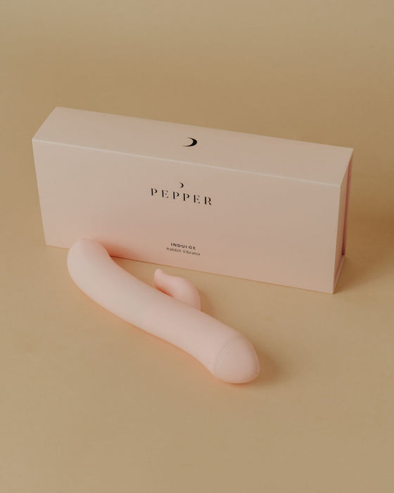 A Pepper Indulge Magnetic Rabbit Vibrator next to its minimalist packaging with the Pepper brand name visible, made with body-safe silicone.