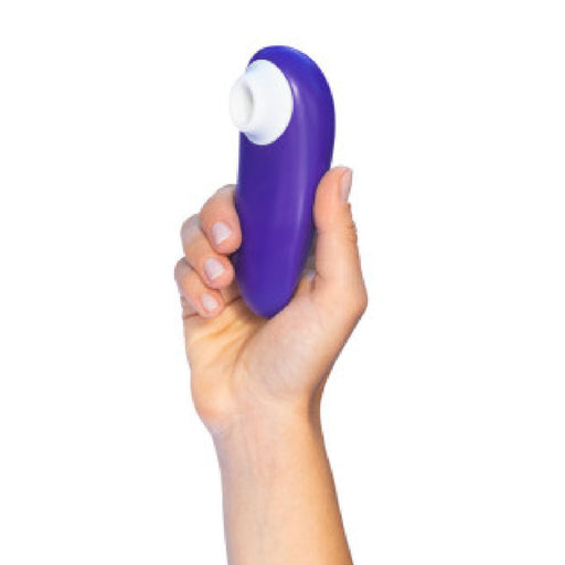 A hand holds the Womanizer Starlet 3 Pleasure Air Clitoral Stimulator, a compact purple oval device with a white circular opening, against a white background.
