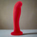 The Jezebel Sleek Curved 6 Inch Red Silicone G-Spot Dildo, featuring a flared suction cup base, stands upright on a light surface against a neutral background.