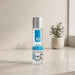 A clear bottle of Jo H2O Original Water Based Lubricant—with a silver cap—sits on a beige countertop. Made with plant-based glycerin and compatible with latex condoms, it’s seen near a small potted plant and softly lit window in the background.