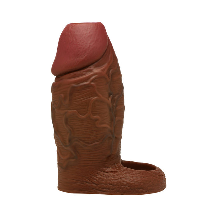 The Jock Girthy Open Ended Silicone Penis Sleeve in Chocolate features a realistic, veined texture, an open-ended tip, and stretchy ball strap, designed to mimic the shaft and head of a penis. Photographed against a white background.