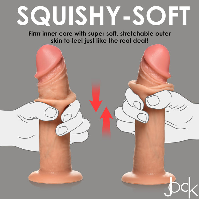The Jock Real Skin Long Vibrating 8 Inch Light Tone Silicone Suction Cup Dildo is squeezed by two hands, showing its soft, stretchable skin and firm core. Text above highlights dual density construction for a lifelike, authentic feel.