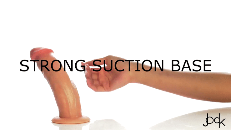 A hand presses down on the Jock Real Skin Thick 8 Inch Light Tone Silicone Suction Cup Dildo with Balls, showcasing its lifelike texture and strong suction base attached to a flat surface. "STRONG SUCTION BASE" appears across the image.