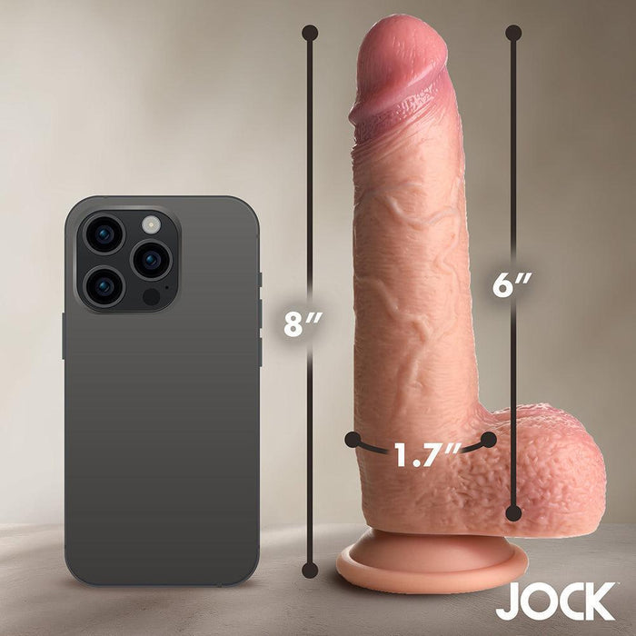 The Jock Real Skin Thick 8 Inch Medium Tone Silicone Suction Cup Dildo with Balls, featuring a lifelike dual-density design, stands upright beside a smartphone. It measures 8" tall, 6" insertable, and 1.7" wide. The JOCK logo is in the bottom right corner.