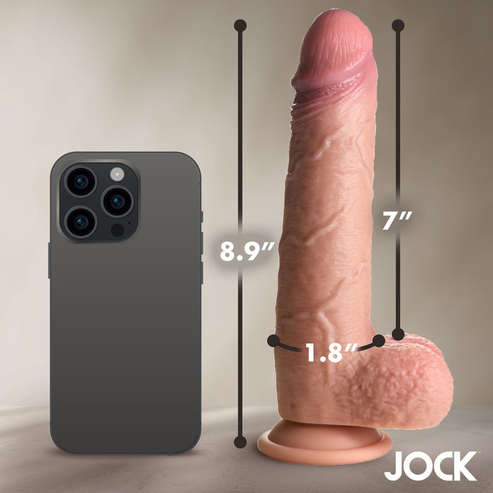 The Jock Real Skin Thick 9 Inch Medium Tone Silicone Suction Cup Dildo with Balls stands upright next to a smartphone for size reference, showcasing its dual density design (8.9" tall, 7" insertable, 1.8" wide), with the "JOCK" brand in the corner.