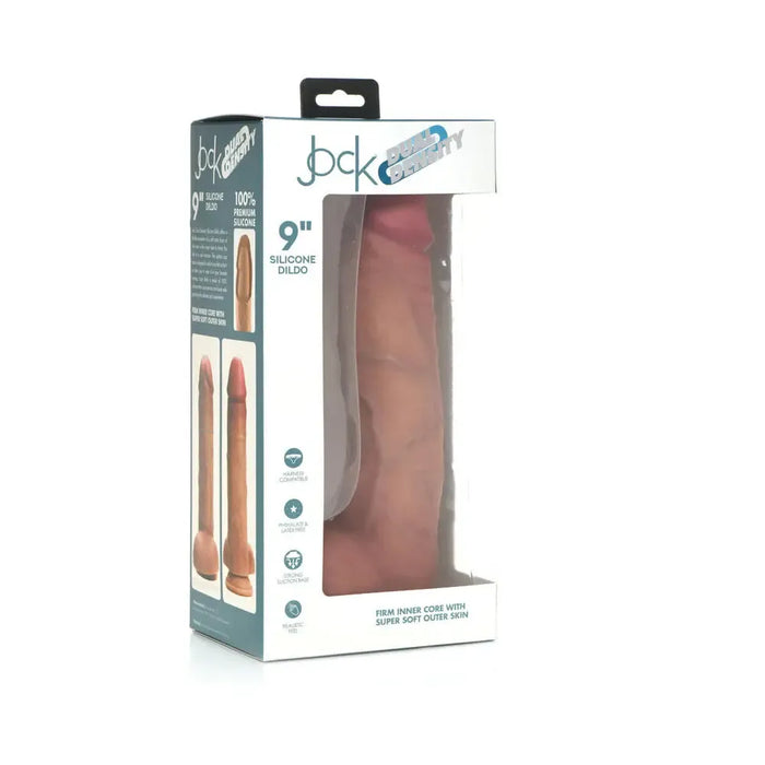 The Jock Realistic Dual Density Huge Silicone 9 Inch Dildo with Balls & Suction Cup is shown upright in clear packaging, displaying its lifelike skin-tone design. The box highlights product details and branding in blue and white.