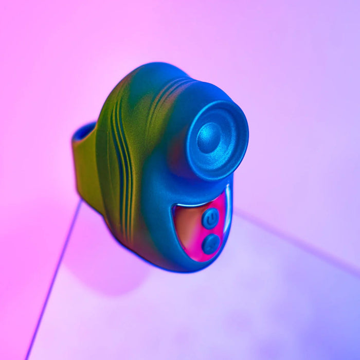 The Kisscool Powerful Mini Clit Taper with Finger Ring, a compact black and teal massager with buttons and a circular opening, sits on a reflective surface under pink and purple lights, showcasing its travel-friendly design.