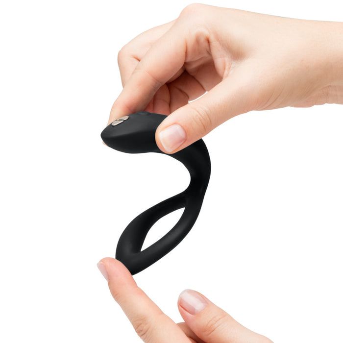 A person holds the Womanizer x We-Vibe Lust & Luxury Collection couples vibrator, bending its flexible black silicone body with both hands against a plain white background.