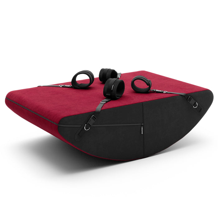Red and black curved rocking positioning cushion with four adjustable black restraint cuffs on a white background.