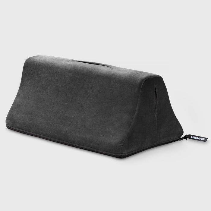 The Liberator Tula – Dual-Toy Sex Cushion for Double the Pleasure is a dark gray, wedge-shaped foam pillow with a soft fabric cover, handle slot, and side tag, ergonomically designed for enhanced comfort and versatile intimate support.