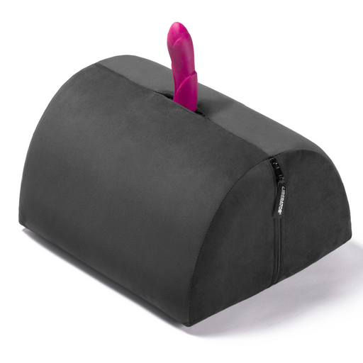 The Liberator BonBon Rideable Sex Toy Mount is a black, semi-cylindrical cushion with a zippered side and a pink silicone sex toy mounted vertically at its center.