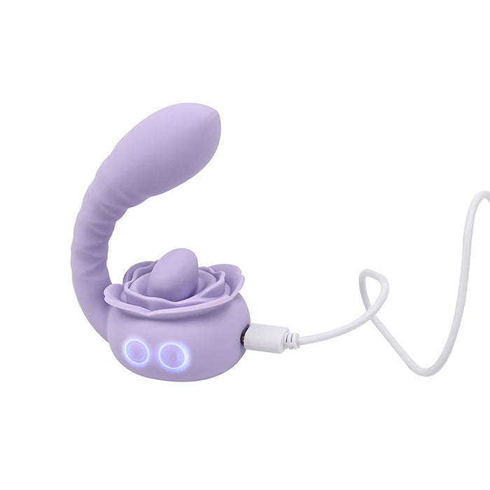 The Lilac Licks Clitoral & G-Spot Vibrator with Tongue Tease features a lavender, rose-shaped silicone design, flexible curved extension, two blue LED lights, and comes with a white charging cable.