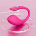 The Lovense Lush 4 Sound Activated Bluetooth Wearable Vibrator, in pink with a curved ergonomic shape and metallic accent, sits on a clear platform with colorful ticks and has a white charging cable attached against a pink background.