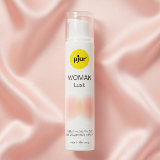 A 15 ml bottle of Lust Orgasm Gel by Pjur Woman, a water-based gel for clitoral stimulation, stands upright on soft light pink satin. The white bottle has a yellow logo and a clear cap.