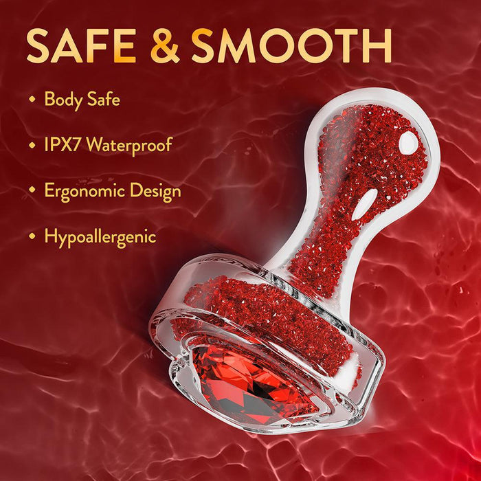 The Lustre Glass Butt Plug with Gem Base & Red Crystals is displayed against a red liquid backdrop. Features noted are body safe, IPX7 waterproof, ergonomic, and hypoallergenic, with its heart-shaped base and rounded design shown.