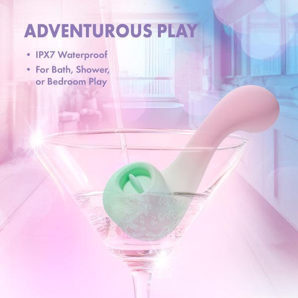 The Melody Double Ended Licking Tongue & G-Spot Vibrator, made from body-safe silicone, rests in a martini glass of water. “ADVENTUROUS PLAY” appears above with “IPX7 Waterproof” and “For Bath, Shower, or Bedroom Play.” Softly blurred background.