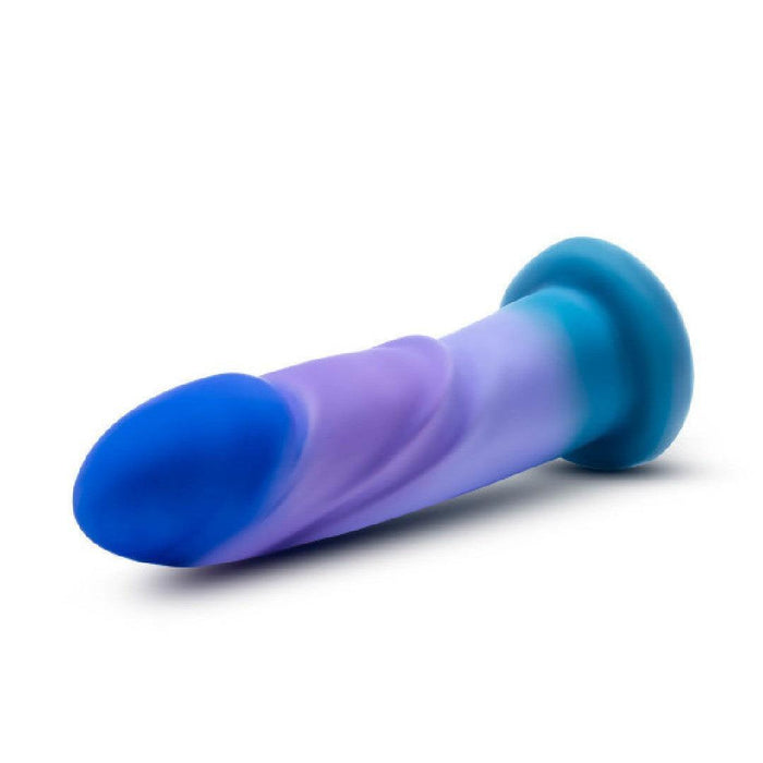 The Midnight Rendezvous Textured 7.5 Inch Girthy Blue Silicone Dildo features a body-safe, blue and purple gradient design, a curved shaft, and a flared base that’s harness compatible—shown against a white background.