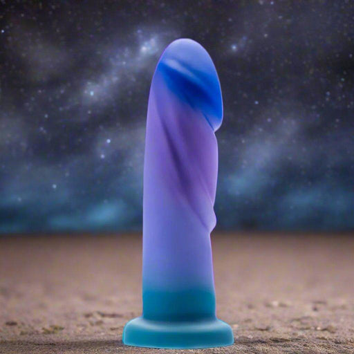 The Midnight Rendezvous Textured 7.5 Inch Girthy Blue Silicone Dildo, crafted from body-safe silicone and harness compatible, stands upright on sand beneath a starry night sky.