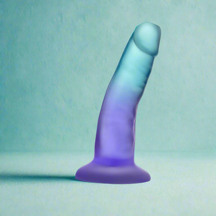 The Morning Dew Slim Small 5 Inch Blue Dildo with Suction Cup stands upright against a light blue textured background, making it an ideal beginner-friendly option for those new to exploration.
