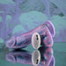 The Mythical Long Thick Vibrating Fantasy Dildo in Pastel Ombre, featuring swirled purple, blue, and pink silicone, rests on a reflective surface next to its white wireless remote against a blurred abstract background.