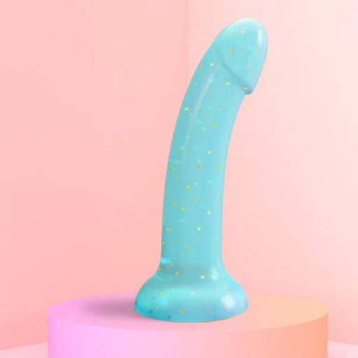 The Nightfall Smooth 7 Inch Teal Glitter Silicone Dildo with Suction Cup stands upright on a pastel pink and orange pedestal against a soft pink background, perfect for prostate or g-spot play.