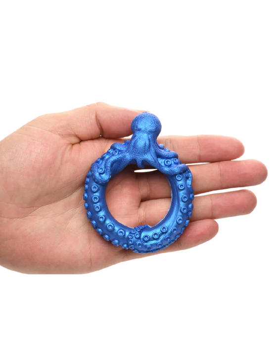 A person holding a blue, waterproof octopus-shaped toy known as XR Brands Poseidon's Octo-Ring Fantasy Cock Ring in their hand against a white background.